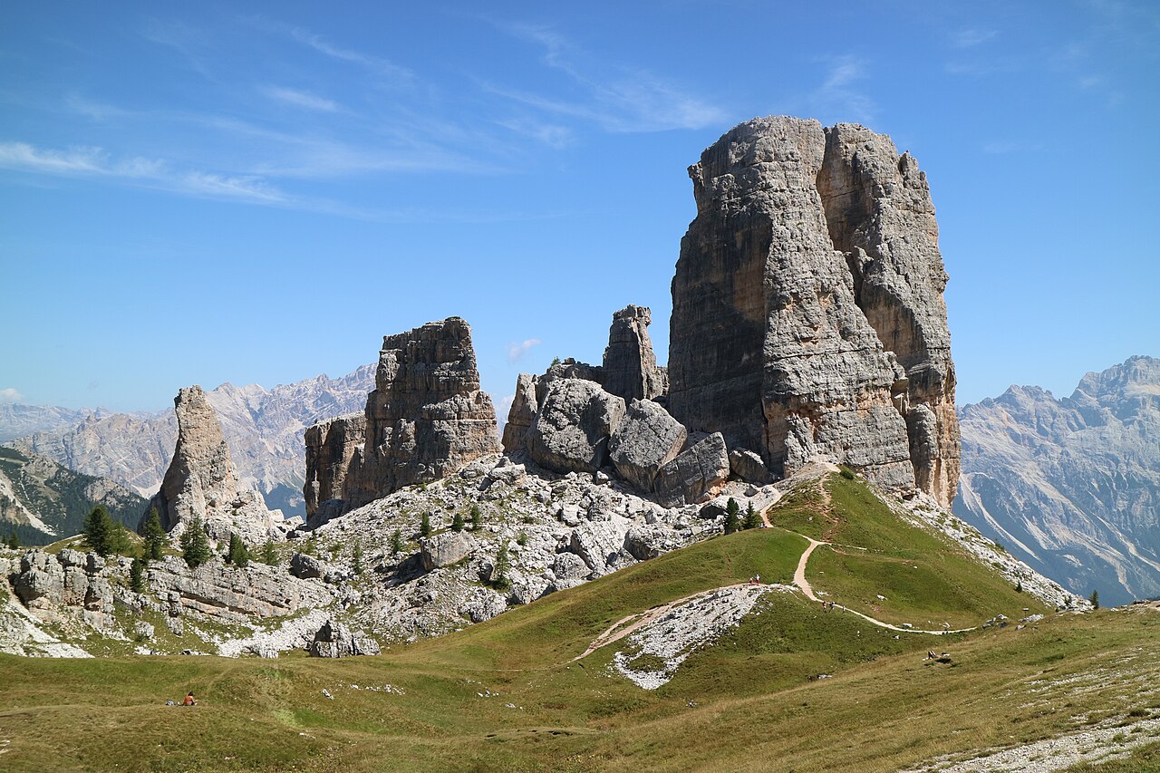 Le Cinque Torri viste da ovest, con la Torre Grande a destra, le torri minori a sinistra e un sentiero tra i prati in primo piano