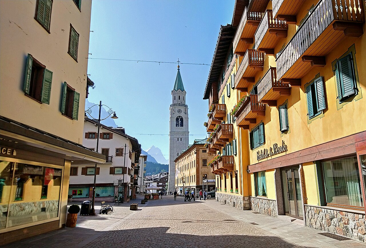 Corso Italia a Cortina d'Ampezzo con le case dai balconi in legno e, in fondo alla via, il campanile della basilica dei Santi Filippo e Giacomo