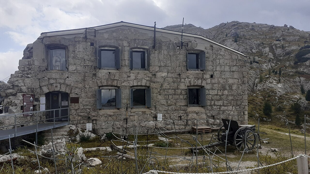 La facciata in blocchi di pietra del Forte Tre Sassi al Passo Valparola, con un cannone d'epoca sul prato davanti
