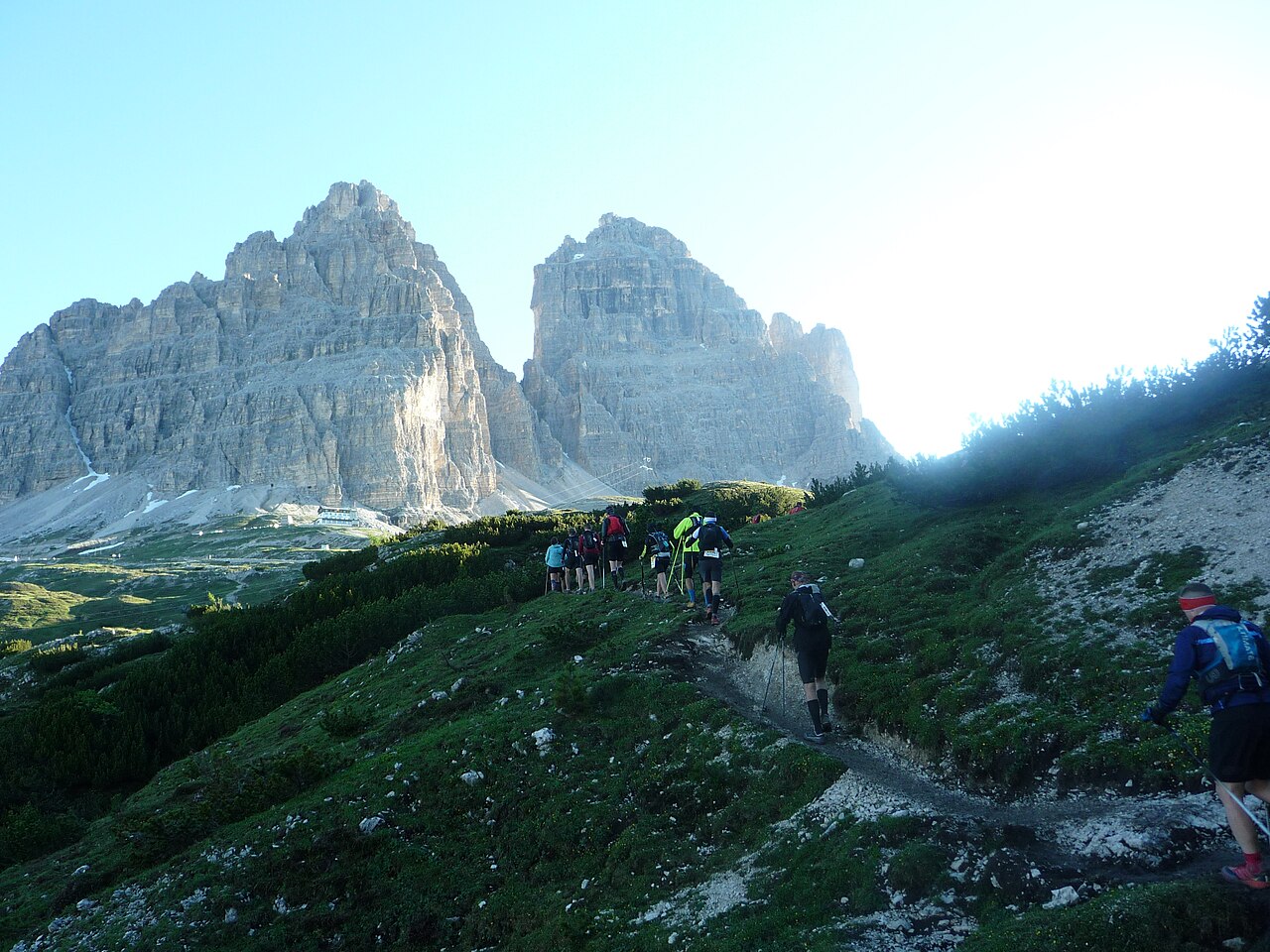 Corridori della Lavaredo Ultra Trail, visti di spalle, salgono un sentiero erboso verso il rifugio Auronzo sotto le Tre Cime di Lavaredo