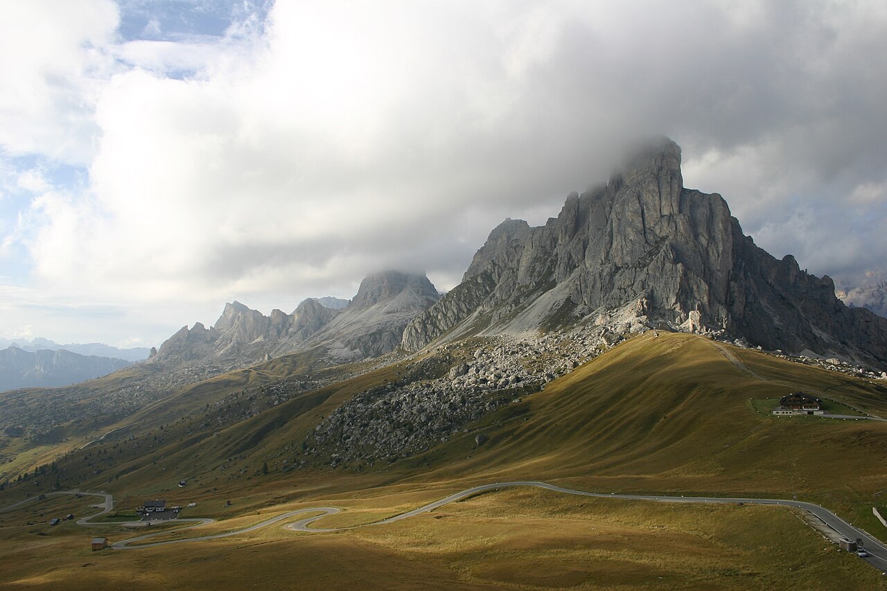 Nuvole basse che avvolgono la cima della Gusela e i prati del Passo Giau, con la strada a tornanti in primo piano