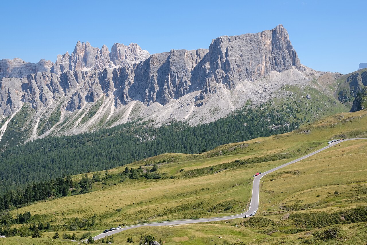 La strada del Passo Giau che sale a curve tra i pascoli, sotto le pareti dolomitiche della Croda da Lago