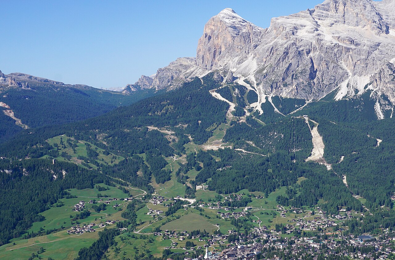 Il tracciato della pista Olympia delle Tofane tra i boschi sotto la Tofana di Rozes, visto dal Faloria a fine estate, con Cortina in basso